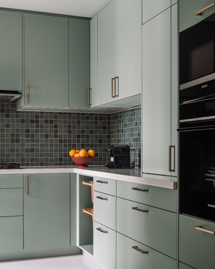 The muted sage green cabinets lend a subdued appeal, while the glossy tile and light countertop enhances the overall visual allure; Photography by Ishita Sitwala