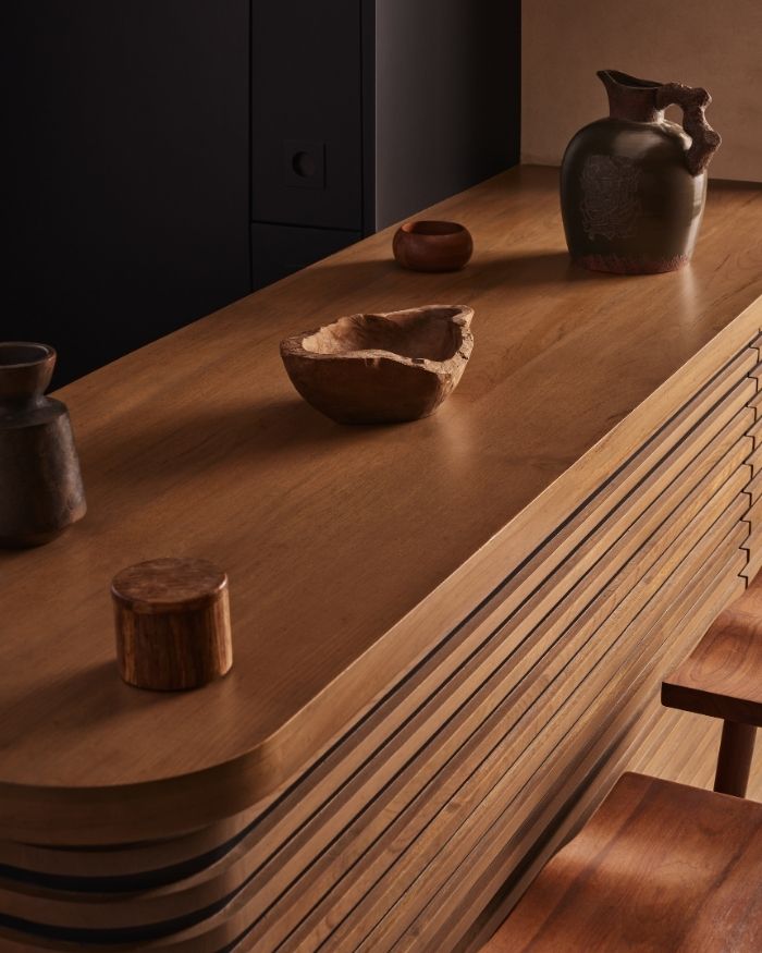 The bar table and chairs echo rich brown tones, while sculptural bowls and tumblers rest gently on the smooth surface; Photography by Yadnyesh Joshi
