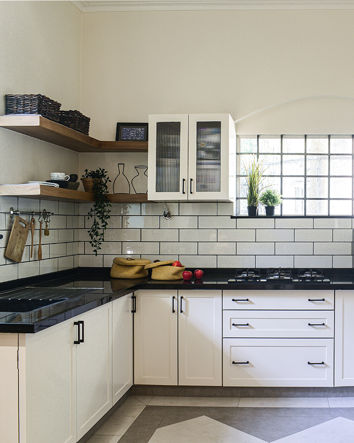 A sunlit kitchen where white cabinetry meets black accents and leafy greens; Photography by Studio Marés