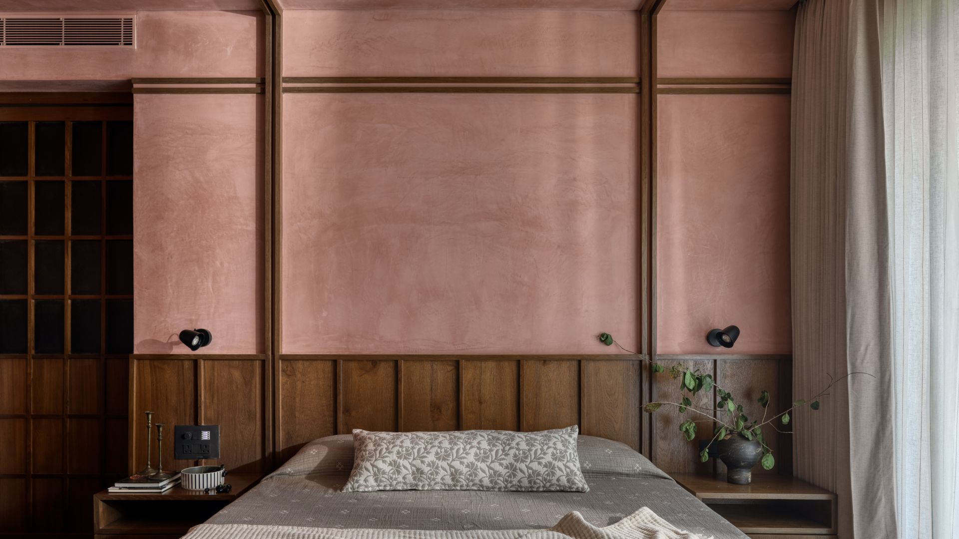 Bedroom with lime-washed pink wall, wooden panel headboard and neutral bedding