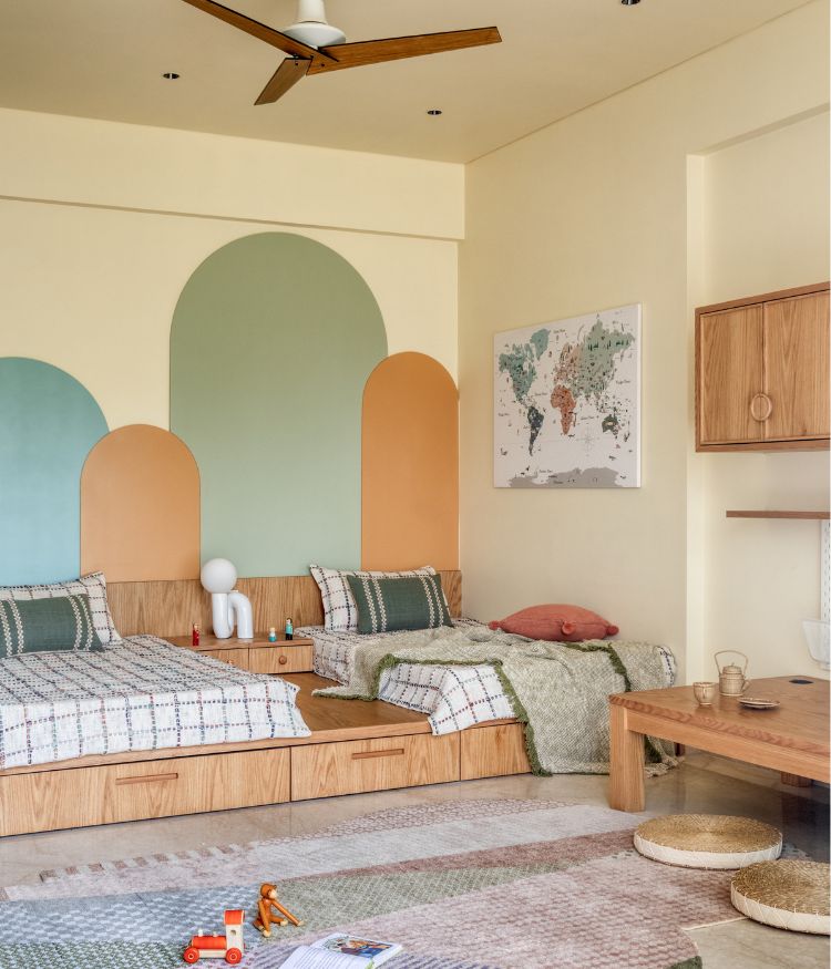 Children’s bedroom with twin wooden beds, pastel arched wall design, study table with neutral furnishing