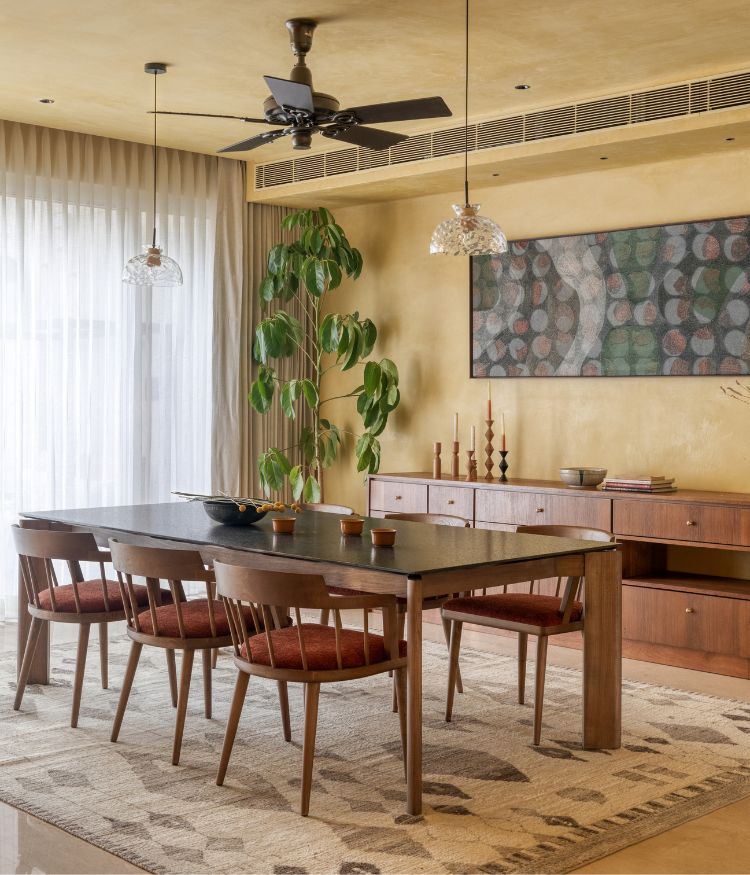 Dining space with wooden table, lime-washed yellow walls, pendant lights and indoor plants