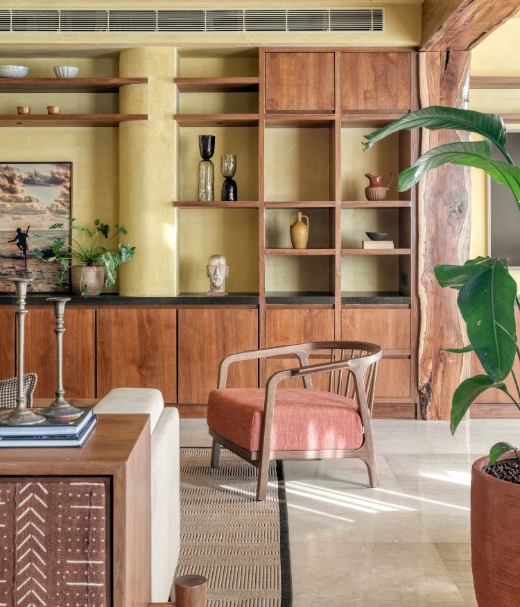 Built-in wooden shelving with decor objects, lime-washed wall finish, indoor plants and upholstered lounge chair