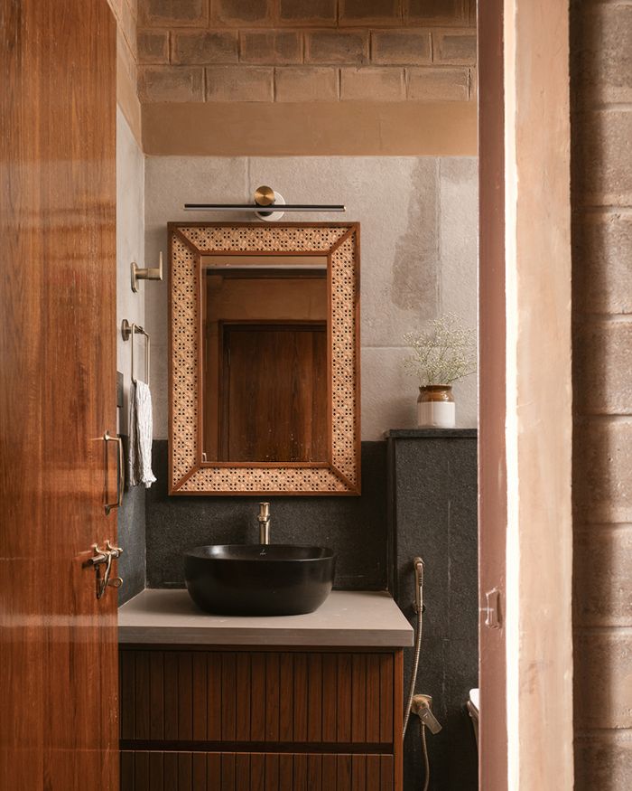 The master bathroom features a bespoke wooden mirror laced with cane, and stone-finished vitrified tiles on the walls and floor; Photography by Nayan Soni