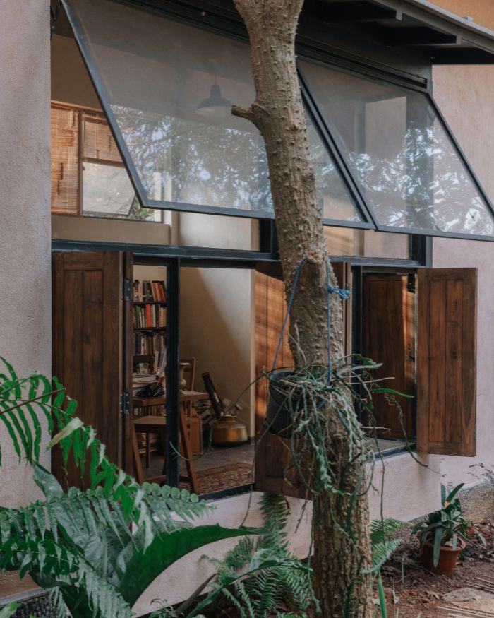 The study window opens into the garden as timber shutters and glass frame the tree beyond; Styled by Imran Ali Khan and Rishad Patel; Photography by Shantanu Starick