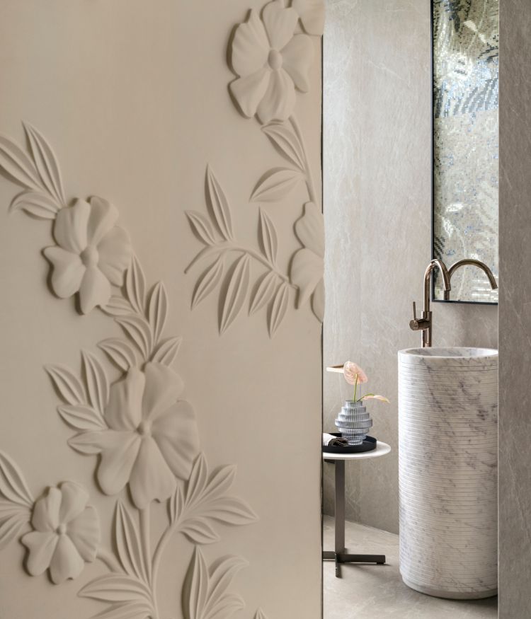 A floral bas-relief plaster wall by Viero leads into the powder room, where a cylindrical Carrara marble pedestal basin sits against grey mosaic tile walls. Sanitaryware by Kohler. Photography by Avesh Gaur; Styling by Shivani Raina