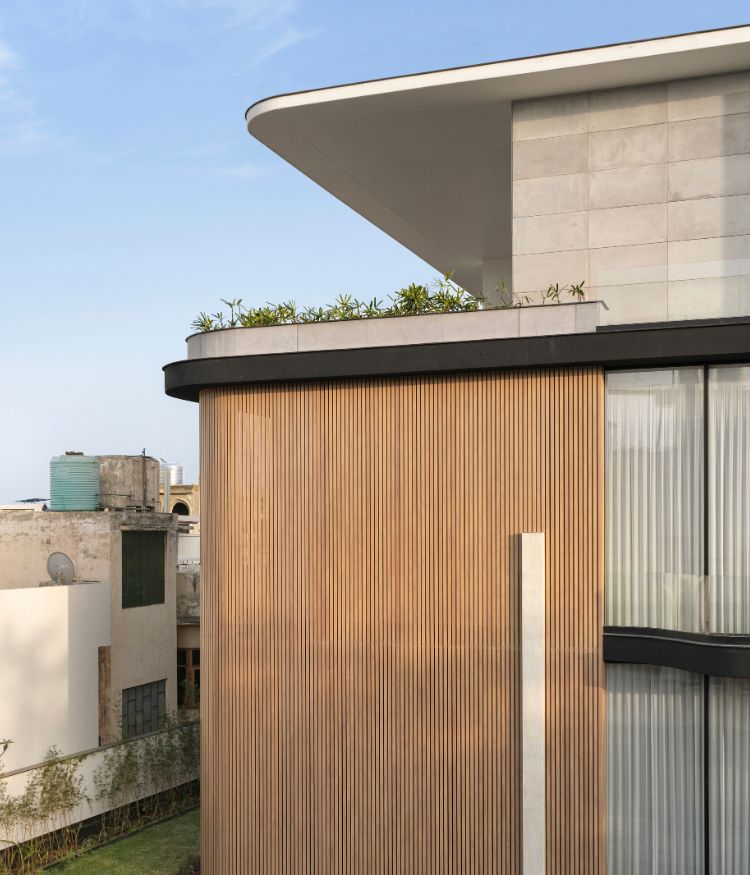 An elevated view of the facade: rooftop planting crowns the structure above a volume of vertical timber battens by Natural Veneers and grey stone cladding by Nexion; Photography by Avesh Gaur