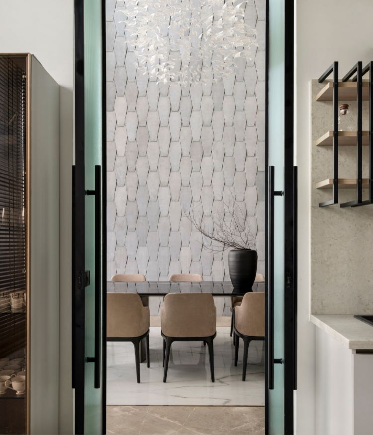 Looking from the kitchen through the glass pivot doors: the dining room's stone feature wall by Roschcrete and chandelier by Panvik Lighting hold the frame. Nexion tiles and Natural Veneers shelving in the foreground. Photography by Avesh Gaur; Styling by Shivani Raina