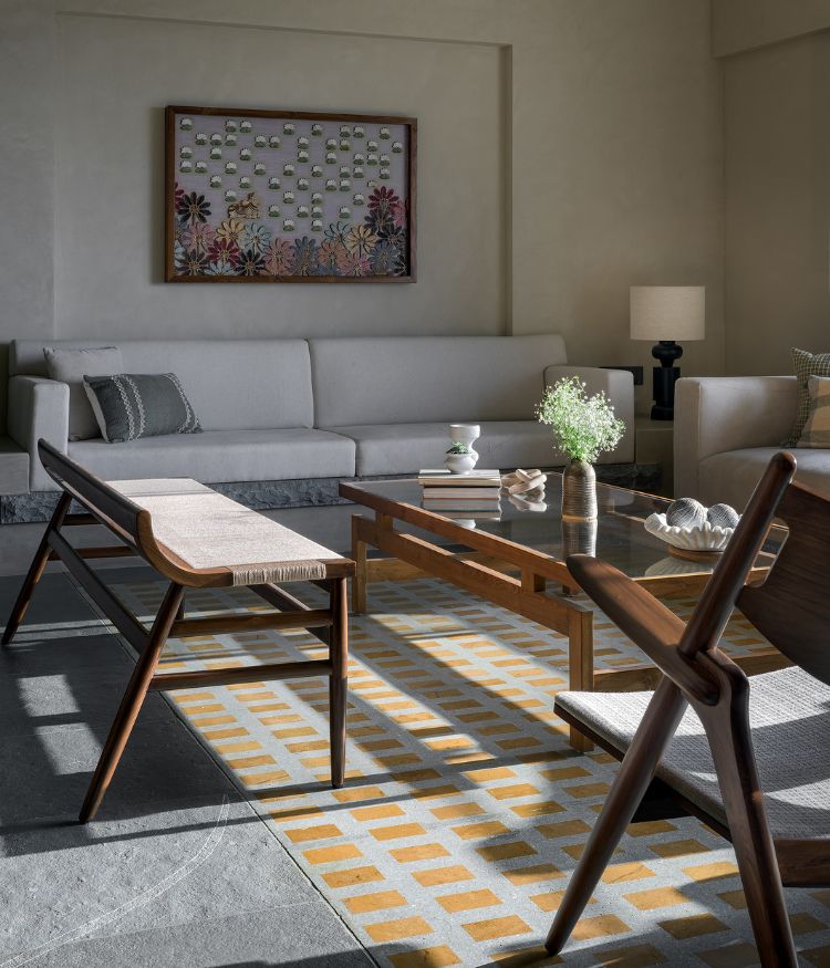 In the living area: a Jaisalmer terrazzo panel by Stonecasa anchors the seating arrangement; a Designbee bench and glass-topped teak coffee table face the linen sofa; a textile artwork by Studio Smitamoksh hangs above; Kota stone flooring with hand-finished tacha detailing and coffered ceiling throughout by Grava Stones. Photography by Hemant Patil
