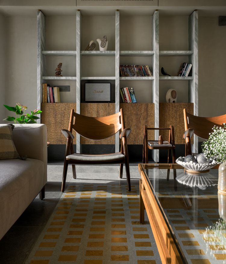 A closer read of the verde green marble bookshelf with woven-front storage cabinets; open shelves hold a Marshall speaker, books and wood sculptures; Designbee teak armchair and glass coffee table in the foreground. Photography by Hemant Patil