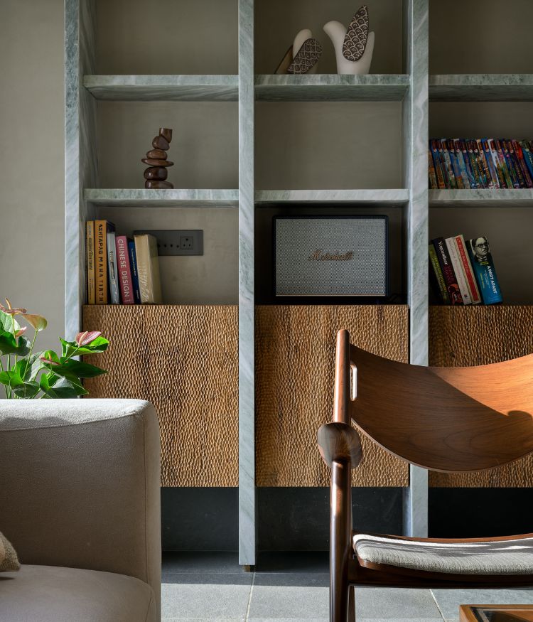 Detail of the verde green marble bookshelf columns and hand-woven cabinet fronts; Studio Smitamoksh sculptures and a Marshall speaker occupy the shelves; a Designbee teak armchair occupies the foreground. Photography by Hemant Patil