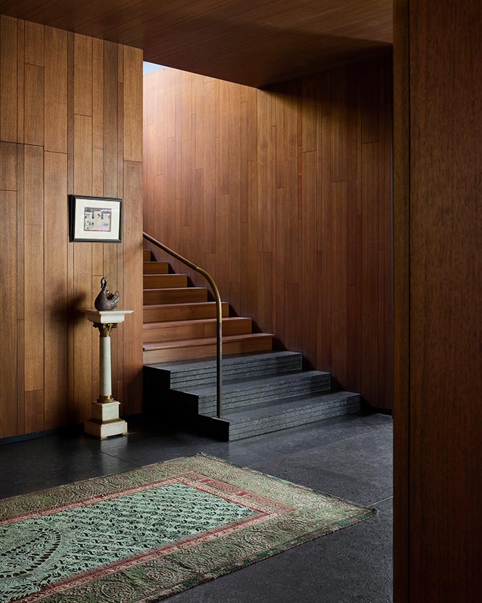 Rich timber tones cocoon the ground-floor staircase and landing, interrupted only by a pedestal from Taherallys and a cerulean Obeetee rug; Photograph by Talib Chitalwala