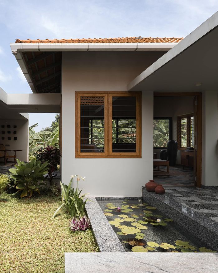 The C-shaped plan reveals its logic here: a planted garden and lily pond form the green centre of the home, granite flooring in a harlequin pattern running between the wings, the tiled roof of the main block rising behind. Styled by Fymin Naif and Nimitha Harith; Photography by Justin Sebastian and Athul Niranjan