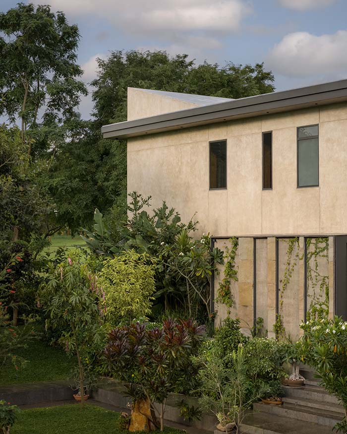 Along a Bengaluru golf course, the home sits within dense greenery, with rugged sandstone surfaces defining its edges; Photography by Ekansh Goel