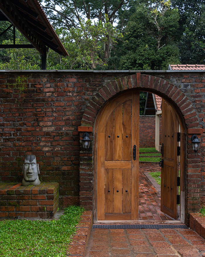 A weathered brick wall curves around a timber arched doorway; Photography by Syam Sreesylam