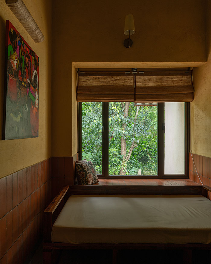 A built-in daybed paired with banana fibre blinds by Ind Eclectik nestles beneath a window, framing the lush green views outside; Photography by Syam Sreesylam