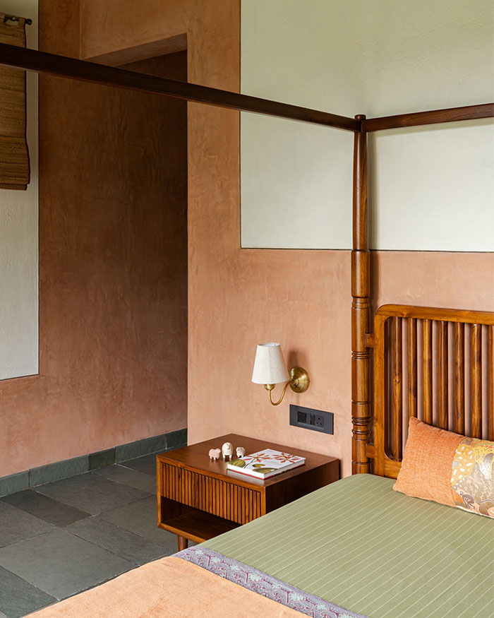 Muted terracotta walls wrap the master bedroom in warmth, paired with a timber canopy bed for a grounded setting; Photography by Syam Sreesylam