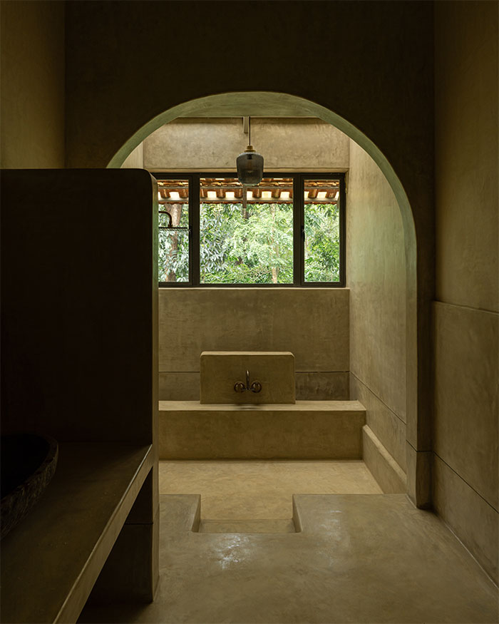 Framed by an arch, the bathroom is carved in smooth plaster. A monolithic basin and windows by Dorfen create a relaxing space; Photography by Syam Sreesylam