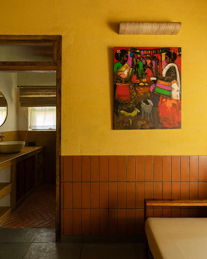 The painting punctuates the yellow wall, bringing life to a passage where wall lights by Sunshine Boulevard and wooden seating keep the palette warm and cohesive; Photography by Syam Sreesylam