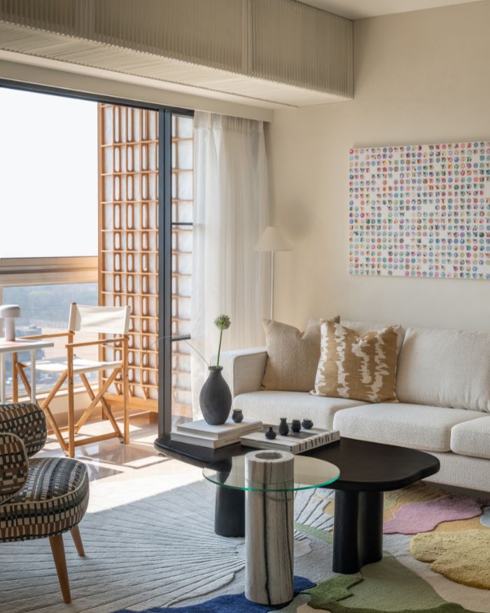The living room maintains the largely neutral palette, splattered with the occasional pop of colour via home accents including wall art from Cultivate Art, a black centre table by Harshita Jhamtani, and a tall floor lamo by Hatsu. Sarita Handa and West Elm cushions adorn the couch by Bo-Concept; Styling by Riddhika Jesrani; Photography by @thekuber @evolve.studio_
