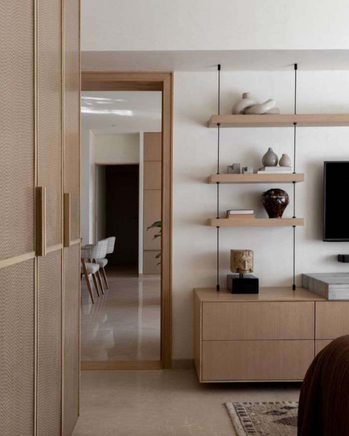 Full-length wardrobes by Arjunvir Gujral Design Studio adorn the bedroom walls on one side, while decor by Mahendra Doshi sits atop a suspended multi-tier floating wall shelf by Material Immaterial; Styling by Riddhika Jesrani; Photography by @thekuber @evolve.studio_