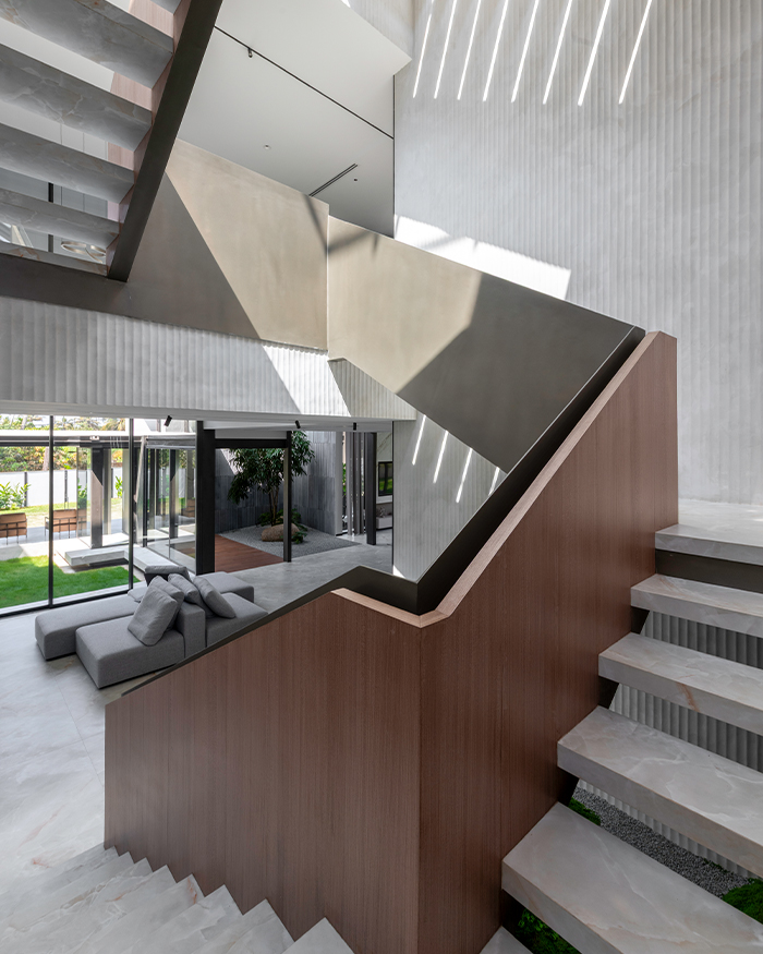 The sculptural staircase cuts through the light-filled interior, creating shifting patterns of shadow across textured walls; Photography by Sebastian Zachariah, PHX India