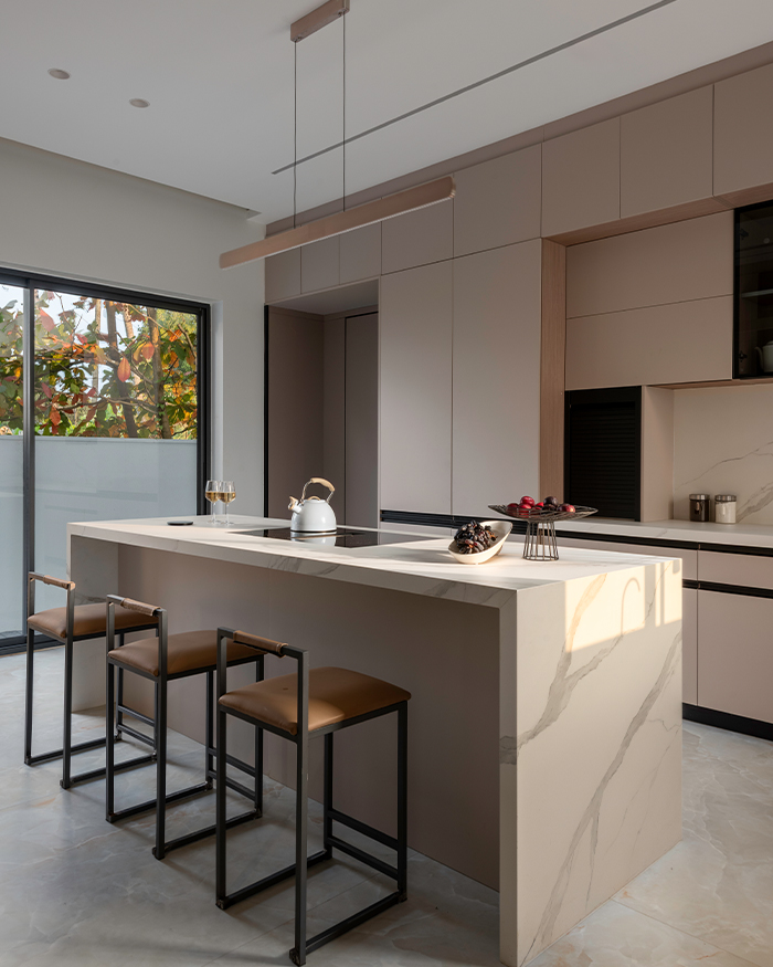 The minimalist kitchen pairs pastel pink cabinetry with a marble island illuminated by natural light; Flooring features Onyx marble and appliances are by Miele; Photography by Sebastian Zachariah, PHX India
