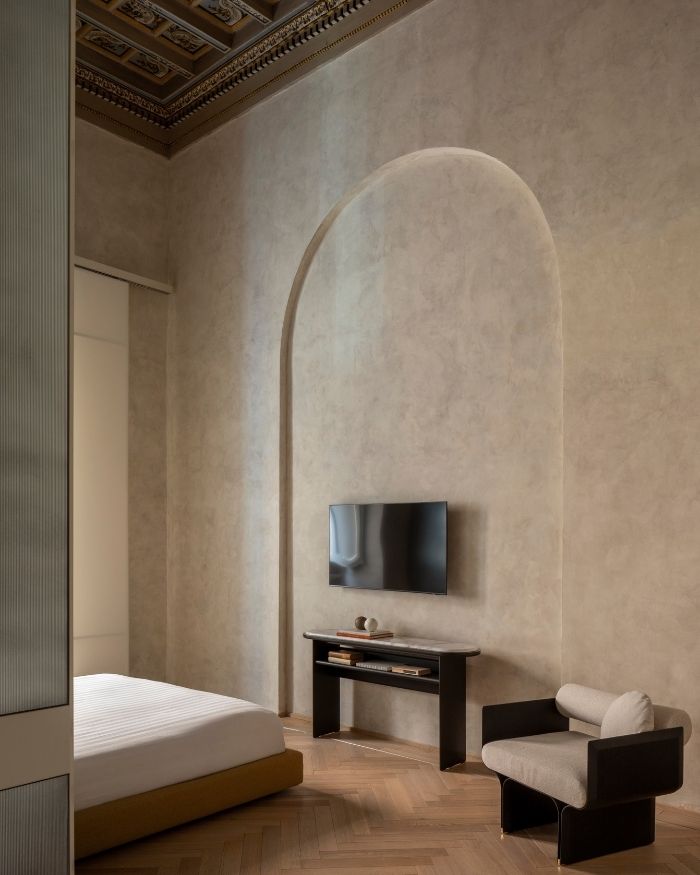 Warm timber herringbone flooring and softly textured walls frame the Stami Lounge armchair by Studiopepe, while the Sensei Console by Tollgard + Castellani lends a sculptural presence beneath the television; Photography by Serena Eller of Eller Studio
