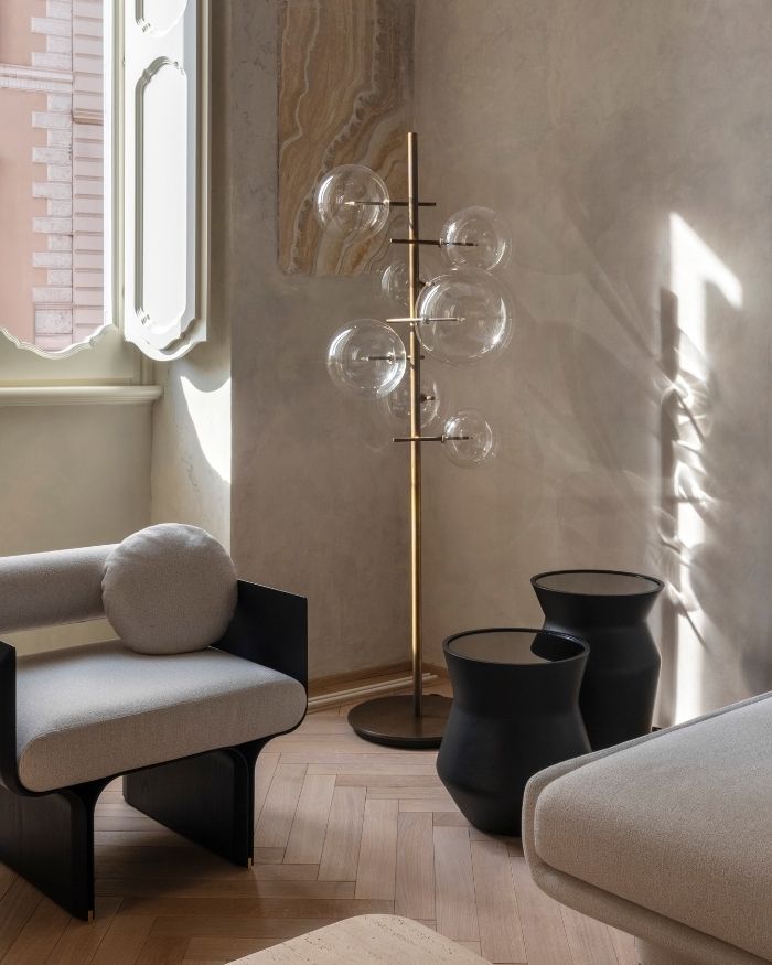 A play of light, shadow and materiality animates this serene corner, where the Bolle Stelo floor lamp by Massimo Castagna stands against softly textured walls, complementing the room’s refined palette of stone, timber and muted neutrals; Photography by Serena Eller of Eller Studio