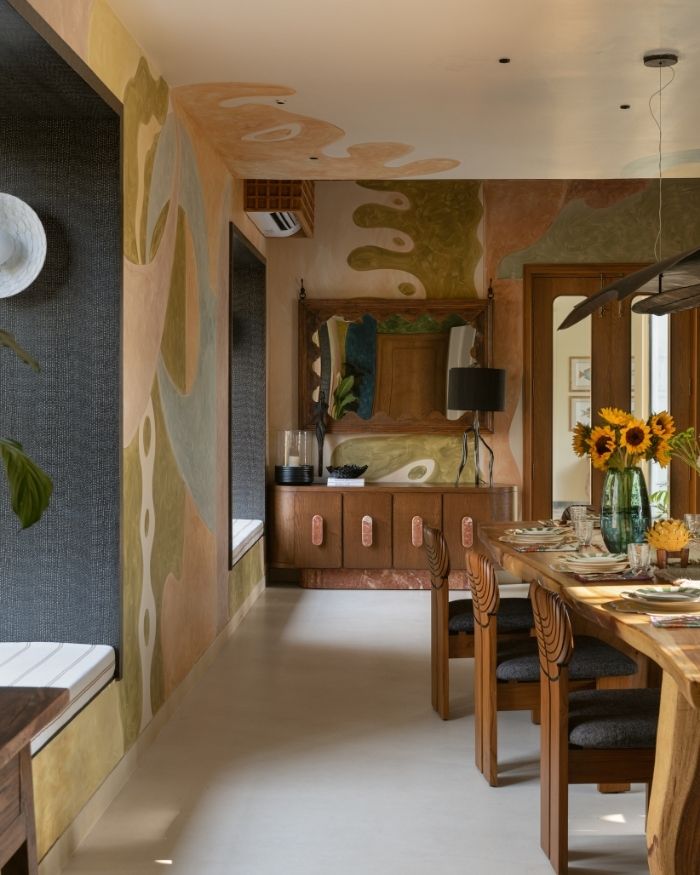A hand-painted mural by Art Bhupi introduces movement across the walls, with furniture by Meher Sra Designs and lighting by Shailesh Rajput Studio; Photography by Nayan Soni
