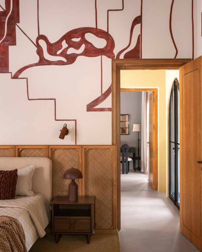 The guest bedroom features a striking red mural, with furnishings by Meher Sra Designs, lighting by The Living Influence, alongside a bed by Altrove; Photography by Nayan Soni