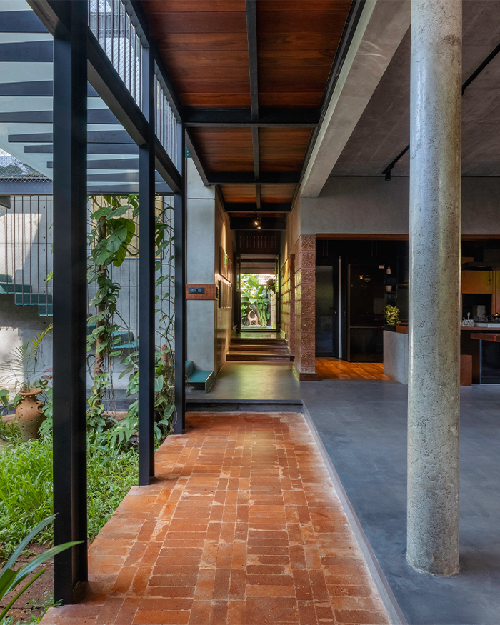 A linear circulation spine weaves through the home, connecting interiors with courtyards and pockets of lush greenery. Exposed brick flooring, concrete, steel, and timber come together to express the project's honest material language and seamless relationship with nature; Photography by Ar. Prashanth Mohan of Running Studios