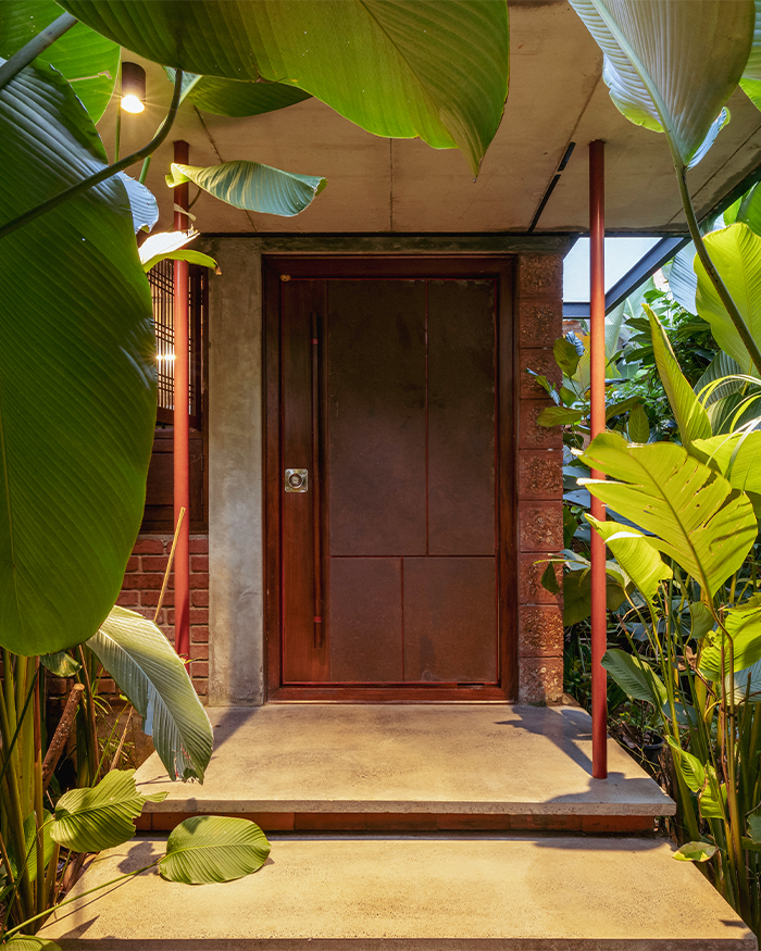 The entrance unfolds through dense greenery, with exposed concrete, laterite and timber elements grounding the home; Photography by Ar. Prashanth Mohan of Running Studios