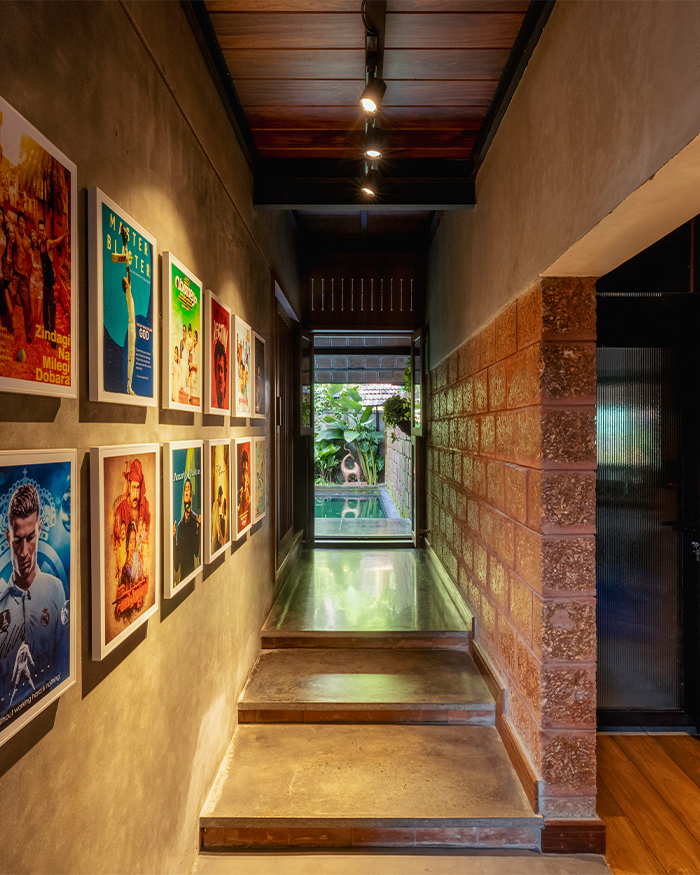 A gallery-like corridor lined with personal memorabilia leads towards a courtyard view, reinforcing the home’s connection to memory and landscape; Photography by Ar. Prashanth Mohan of Running Studios