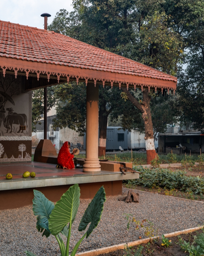 The carved lace border overhead, a wood fire at her feet, a woman in red at the chulha — this pavilion wasn't designed
around furniture, it was designed around this exact moment; Styling by Priya Goyani; Photography by Tarun Hirpara