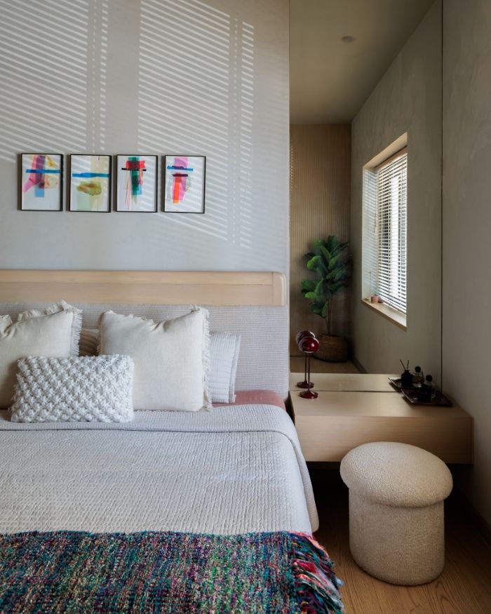 Four abstract mixed media works by Julius Das animate the calm bedroom, where a woven Jaipur Rugs runner, boucle pouf and soft neutral bedding balance vivid colour with quiet, layered texture; Photography by Wabi Sabi Studio