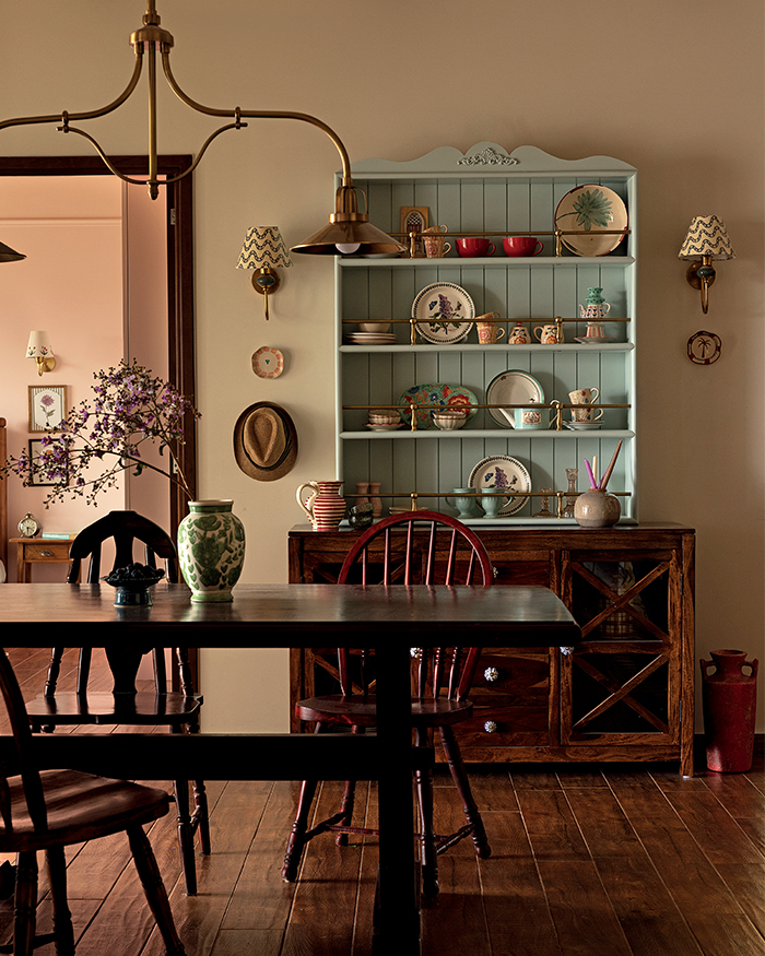 An open cabinet painted in a soft pastel blue displays serveware, while a curved chandelier from Orabel Brass hangs above the dining table;
Styling by Shivani Raina ;Photography by Phosart Studio