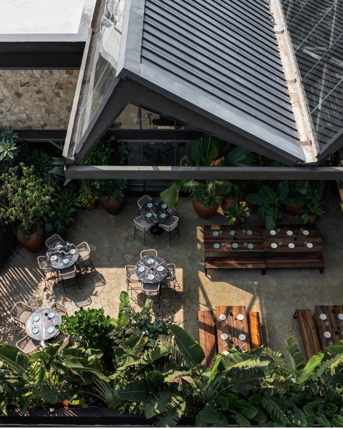The 30-foot cantilevered outdoor area, threads structural trusses along the perimeter to maintain continuity of the roof form, while greenery and blue plating carry the indoor language outside; broken slate flooring and grit-finished parapet walls add to the industrial feel.