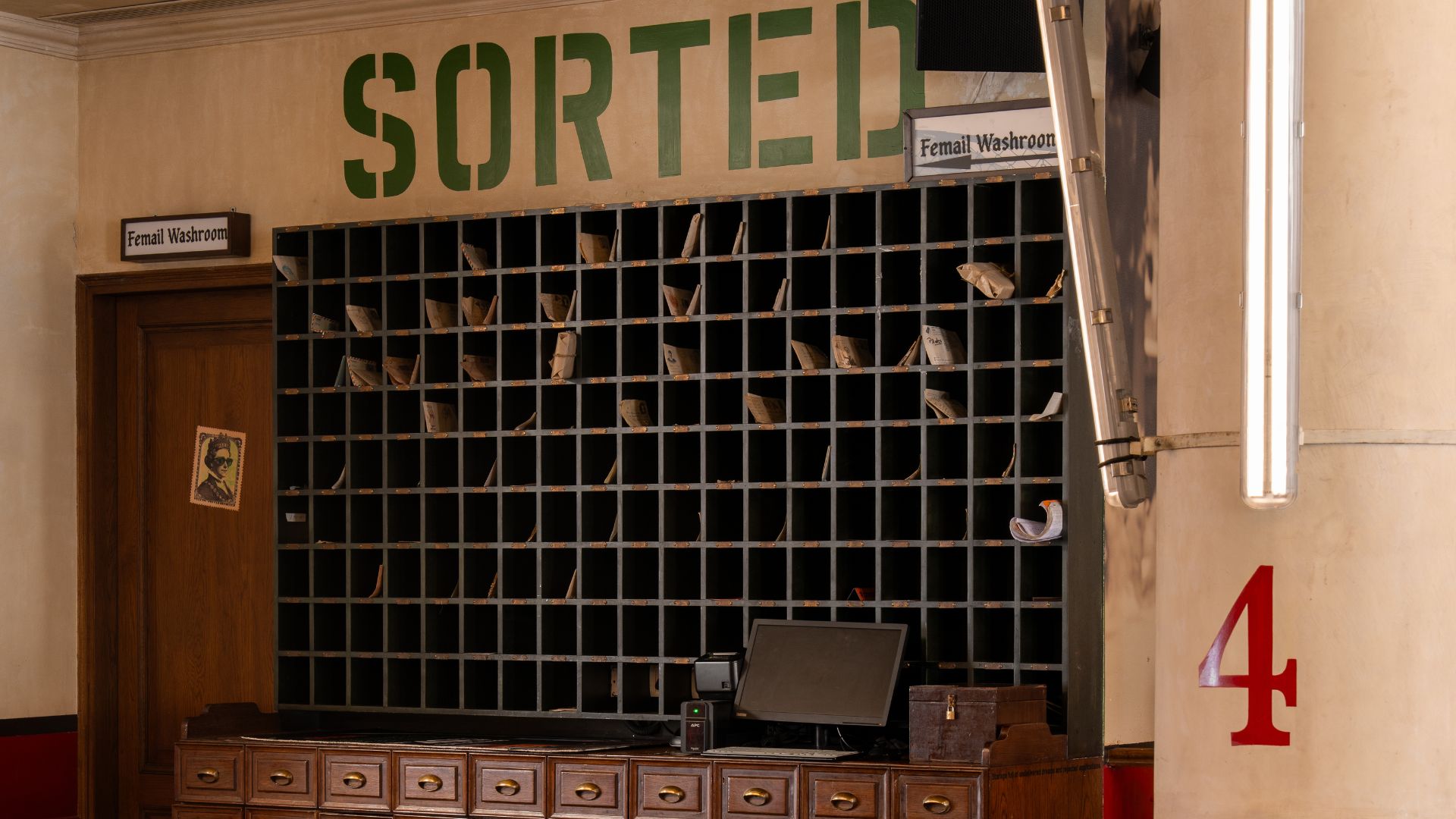 Stenciled letters spell Sorted above a wall of pigeonholes stuffed with paper and a nearby door to the a restroom is marked Femail