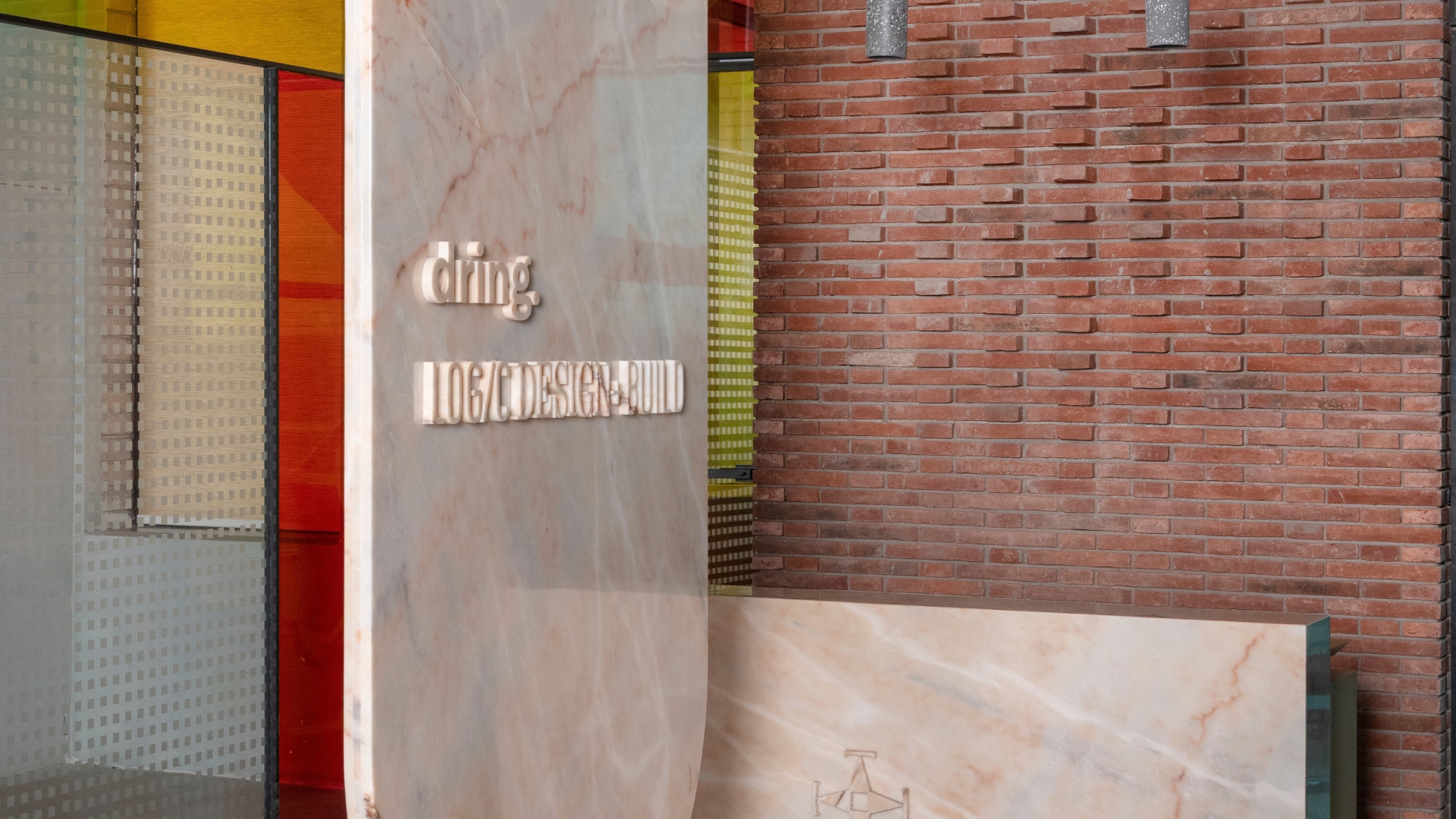A curved Michelangelo marble desk and birch ply base and brass signage at the entrance to Logic Design + Build's Gurugram office
