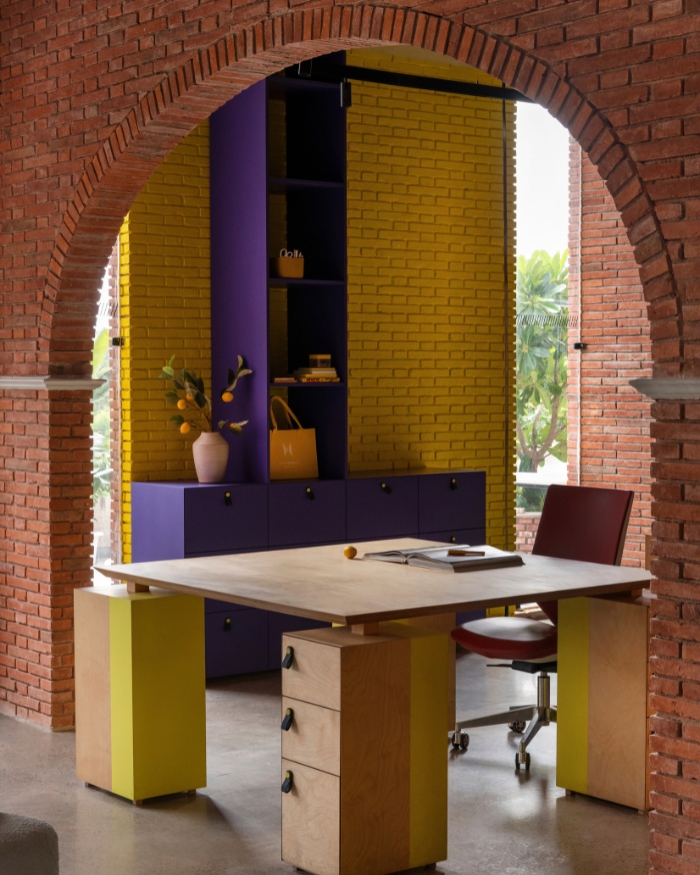 A yellow brick arch and custom purple shelving holding books, boxes and a citrus branch