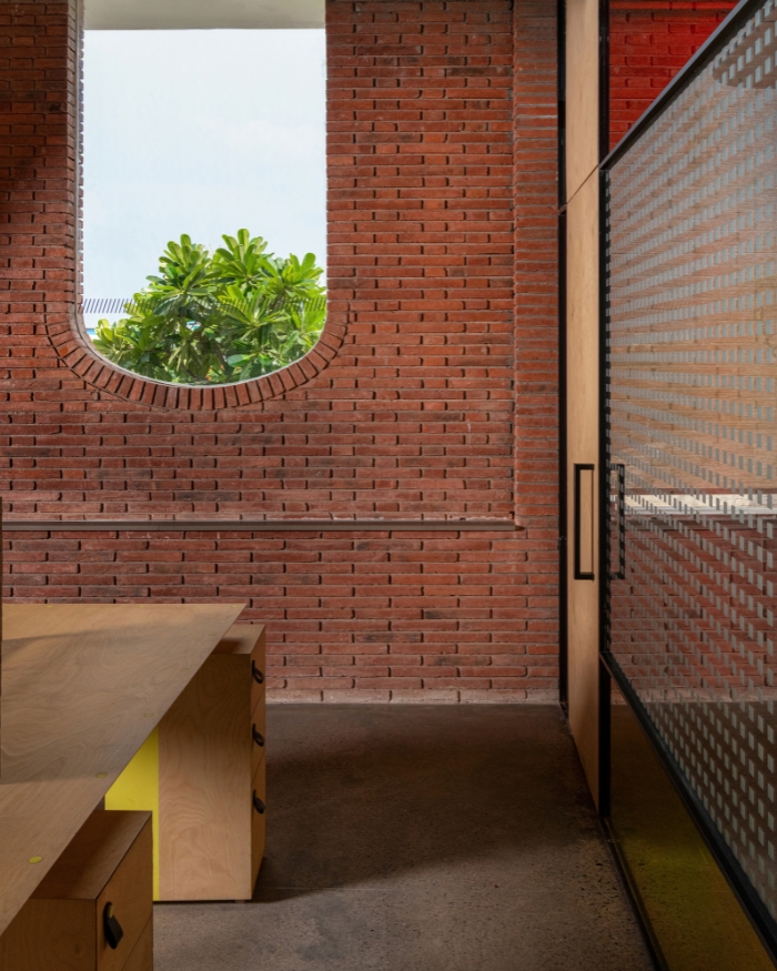 A desk with citron yellow drawers beneath a deep brick opening, the dot-patterned glass door alongside catching a glow of red from the room beyond
