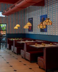 The interior blends rich burgundy pod seating by the KK contractor with deep blue accents, patterned wall artwork by Pranay and warm terracotta ceilings. Lighting from The Peacock Life completes the bold, immersive dining environment; Styling by The Orange Lane; Photography by Kuber Shah