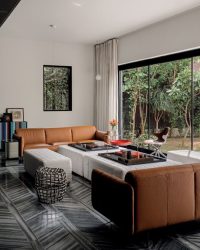 Muslin drapes with leather piping from Tulio calmly frame the glazing, drawing the eye toward the greens beyond. At the
far end, a red side table by AKFD and a striped credenza, designed by Architecture Discipline and crafted by Ahuja Furnishers, introduce moments of colour and texture to animate the living space; Photography by Ishita Sitwala