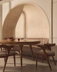 Soft light brushes the plaster arch, tracing gentle curves above a long wooden table. Curved-backed chairs and a ridged banquette hug the walls, their buttery leather and warm tones inviting slow, lingering meals; Photography by Yadnyesh Joshi